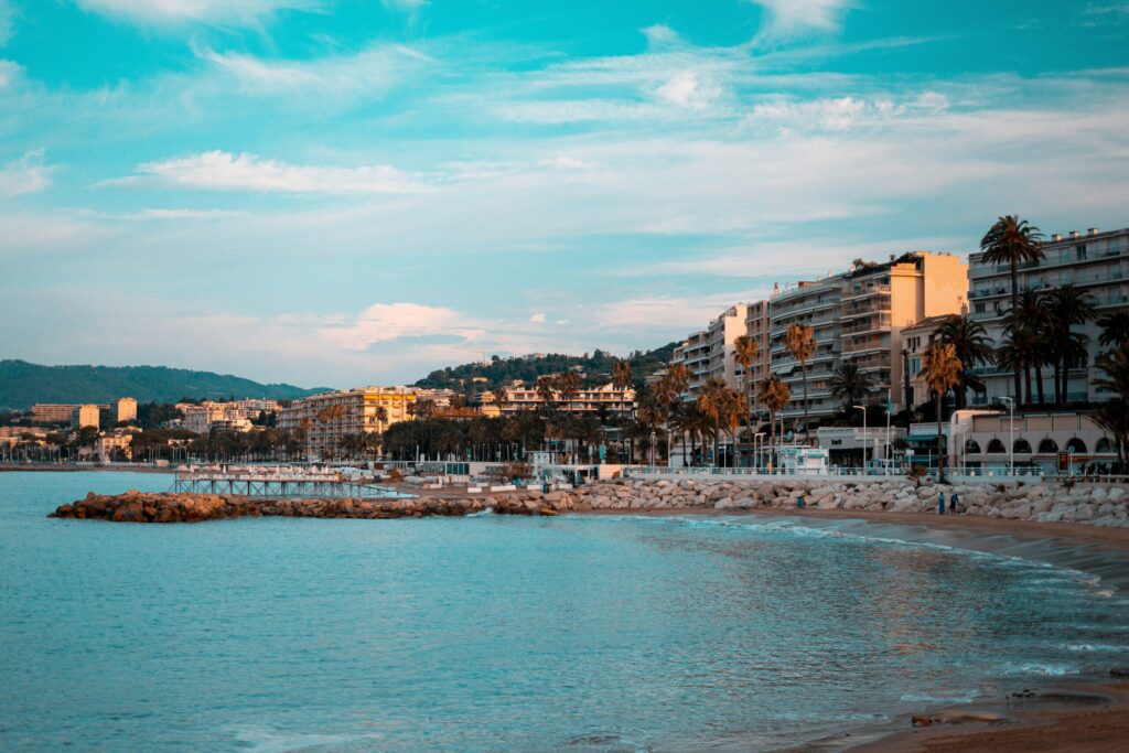 A coastal town with palm trees, hotels, and a boardwalk along the Mediterranean Sea in the evening sun.