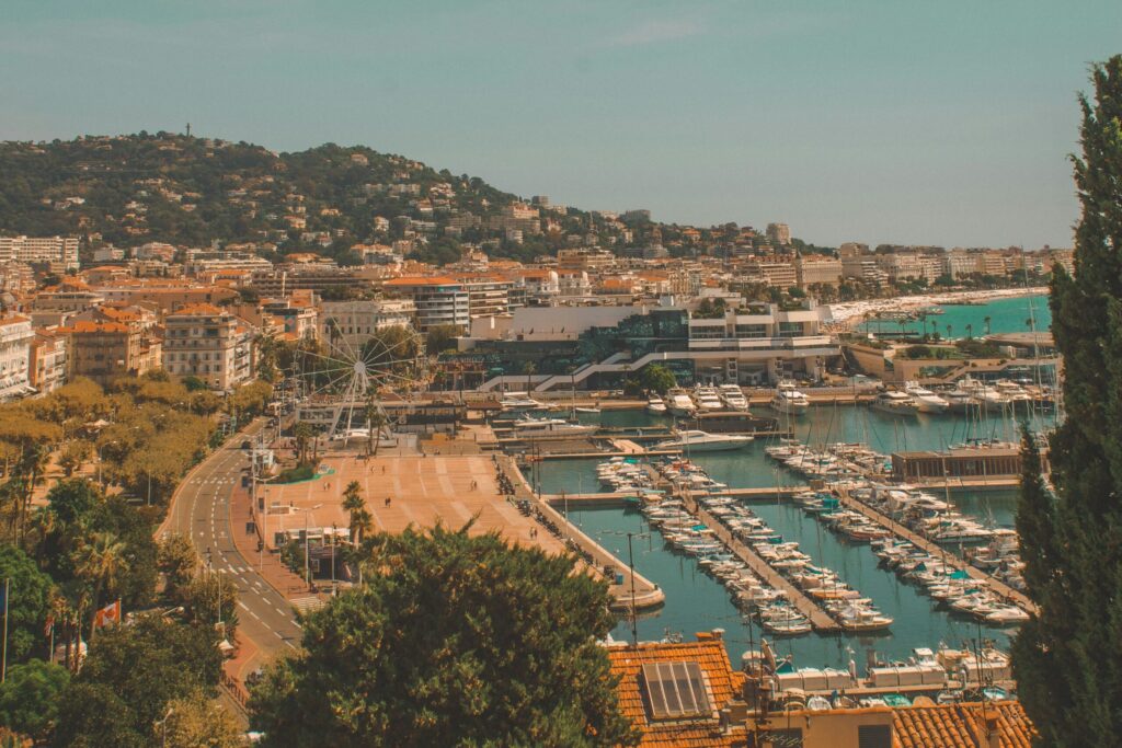 A view of the harbor with yachts, the beach, and the town’s charming houses, with mountains in the background.