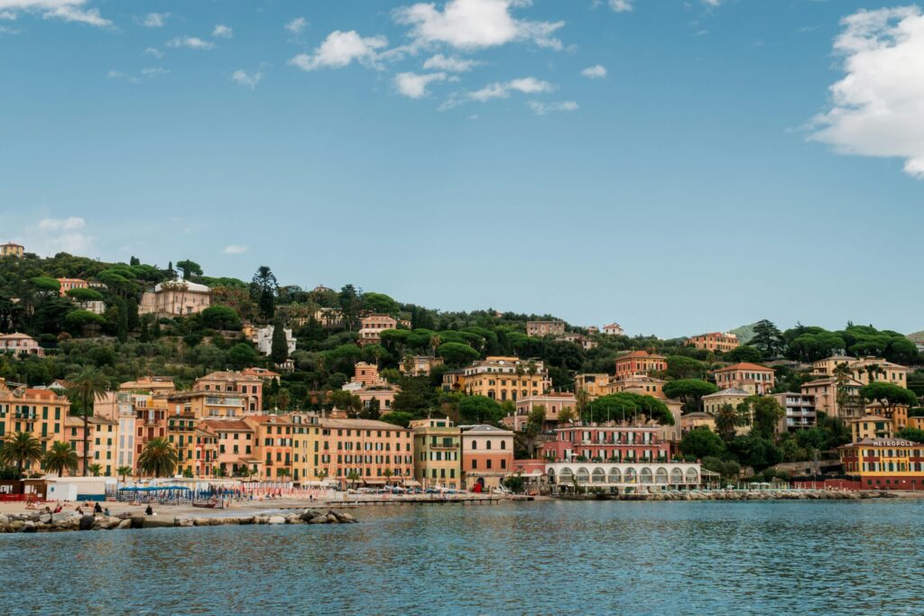 Billede af kysthuse i Seborga, Italien, med farverige bygninger og grønnetræer, og vand for foden af bakken.